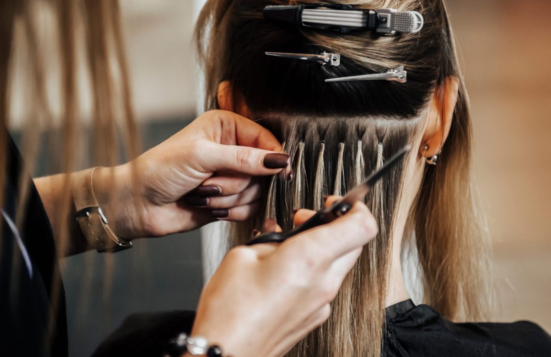 The hairdresser does hair extensions to a girl, a blonde in a beauty salon. Professional hair concept